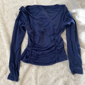 Mörkblå långärmad topp med rynkade sidor - Säljer en mörkblå långärmad topp med figurnära passform och snygga rynkade detaljer längs sidorna. Perfekt för dig som vill ha en enkel men ändå stilren look. Toppen har en rund halsringning och är gjord i ett mjukt, stretchigt material.