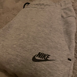 Grå mjukisbyxor från Nike - Säljer ett par grå mjukisbyxor från Nike med svart logga på benet. Byxorna har resår i midjan och är tillverkade i mjukt material, perfekta för en avslappnad stil eller träning. Nyskick, använt ca 1 gång! Priset går absolut att diskutera, tveka inte att kontakta angående frågor!
