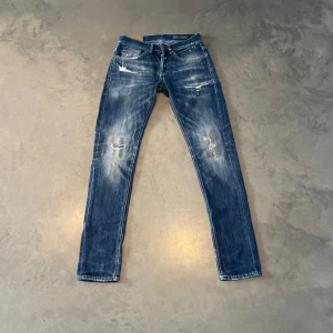 Dondup Jeans - Säljer ett par blå jeansbyxor från Dondup med slitningar och lätt tvättade detaljer. Klassisk femficksmodell med raka ben och låg midja. Snygga kontrastsömmar och diskret logga bak i midjan. Väldigt snygga byxor och perfekt passform! Orginal pris mellan 2000-3000kr