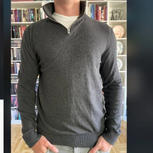 Mörkgrå halvzip-tröja från Jack & Jones - Säljer en stilren mörkgrå tröja från Jack & Jones med halv dragkedja och hög krage. Tröjan har ribbade muddar vid ärmslut och nederkant, perfekt för lager-på-lager.