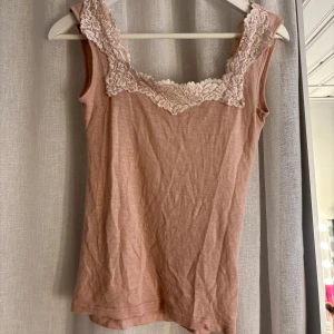 Rosa linnetopp med spets från WOLBIA - Söt ljusrosa linnetopp från WOLBIA med bred spetskant längs ringningen. 