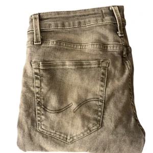 Beige jeans från Jack & Jones - Säljer ett par gråa jeans från Jack & Jones med klassisk femficksdesign och diskreta sömmar på bakfickan. Byxorna har normal passform och är tillverkade i ett mjukt jeanstyg som passar till många olika stilar.