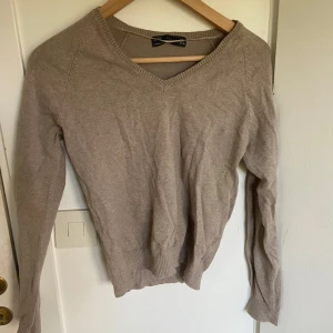 Beige v-ringad tröja från Zara - Storlek L men sitter som en XS! Säljer en beige v-ringad tröja från Zara i mjuk bomulls- och nylonblandning. Tröjan har långa ärmar och ribbade muddar vid ärmslut och nederkant. Perfekt för lager-på-lager under kyligare dagar.
