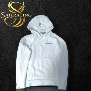 Vit hoodie från Sail Racing - Säljer en stilren vit hoodie från Sail Racing med logga på bröstet. Tröjan har huva och en stor magficka framtill. Perfekt för en avslappnad look.