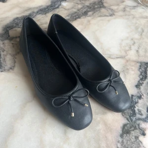 Svarta ballerinaskor❣️ - Säljer ett par klassiska svarta ballerinaskor från H&M med söt rosettdetalj framtill. Skorna har rund tå och platt sula, perfekta för en stilren och enkel look. Passar till många olika outfits! Säljer eftersom att de var för stora på mig, jag skulle säga att skorna passar som 37/38!🥰❤️