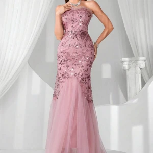 Rosa axelbandslös långklänning med paljetter - Elegant axelbandslös långklänning i ljusrosa med glittriga paljettdetaljer upptill och tyllkjol. Klänningen har en figurnära passform upptill och vidd nertill, perfekt för festliga tillfällen.