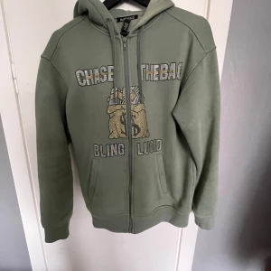 Grön hoodie med dragkedja från Bling Lucid  - Säljer en grön hoodie med dragkedja från Bling Lucid. Den har ett snyggt rinestone tryck fram och är i väldigt bra skick. Säjs då det inte används, hör gärna av dig vid funderingar. Mvh Rufus 😄