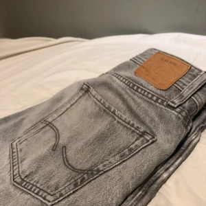 Grå jeans från Jack & Jones - Snygga grå jeans från Jack & Jones med en relaxed passform. De har en klassisk femficksdesign och knappar i gylfen. Perfekta för en avslappnad stil. Priset ej hugget i sten mvh Linus🤠