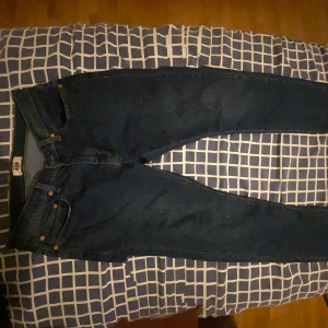 Mörkblå jeansbyxor från Levis - Säljer ett par klassiska mörkblå jeans från Levis med raka ben och fem fickor. Byxorna har orangea sömmar och metallknappar. Perfekta till vardags och passar till det mesta.
