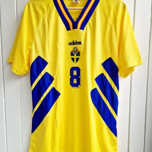 Klas Ingesson - Sverige VM 1994 - Säljer Klas Ingessons klassiska svenska hemmamatchtröja från VM 94 i USA. Tröjan är en remake i nyskick med broderade emblem mm av högsta kvalité.   Large, normal i storleken.  Skickas inom 24 h.  #fotboll 