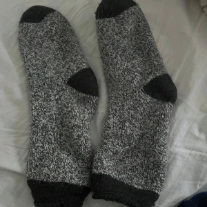 Grå  stickade sockor - Mysiga grå stickade sockor med mörkgrå förstärkning på tå, häl och mudd. Perfekta för kalla dagar och håller fötterna varma. Tjockt och mjukt material som känns skönt mot huden.