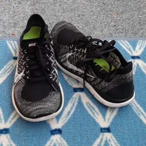 Nike Flyknit svartvita sneakers - Säljer ett par Nike Flyknit sneakers i svart och vitt med stickad ovandel och vit sula. Skorna har klassisk snörning och en flexibel, lätt design med grönt innerfoder. Perfekta för dig som gillar sportig stil. Skor är mycket lätta och bekväma i bra skick. Finns inga skador eller fel. 