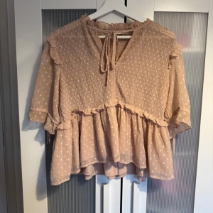 Beige blus med volang och knyt - Söt beige/rosa blus med små prickar, volangdetaljer och knyt framtill i halsen. Blusen har trekvartsärm med knytband och en luftig, lös passform. Skriv privat för fler bilder 🩷