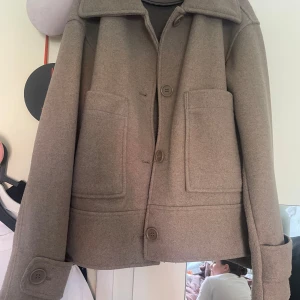 Beige ulljacka med stora fickor - Säljer en beige jacka i ull med stora framfickor och knappar. Andvänd 3 gånger, säljs ej längre
