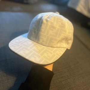 Vit Fendi keps  - Säljer en stilren vit keps från Fendi. Kepsen är i riktigt fint skick säljer på grund av att den inte passar min huvudform bra.