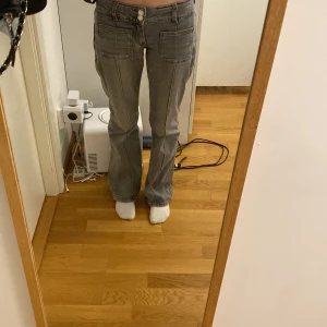 Grå jeansbyxor från Gina Tricot - Säljer ett par grå jeansbyxor från Gina Tricot med raka ben och stora fickor framtill. Byxorna har normal passform och är perfekta för en avslappnad stil. Klassisk femficksmodell och stängs med dragkedja och knapp.