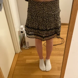 Leopardmönstrad kjol från Lindex - Säljer en leopardmönstrad kjol från Lindex med smock i midjan och volangdetaljer. Kjolen är kort och har ett snyggt fall med flera lager. 