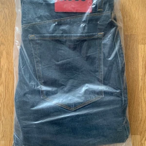 Mörkblå jeans från Hugo Boss - Säljer ett par klassiska mörkblå jeans från Hugo Boss med raka ben och snygga kontrastsömmar. Jeansen har fem fickor och stängs med dragkedja och knapp. Perfekta för en stilren look.