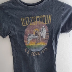 Svart Led Zeppelin t-shirt - Cool svart t-shirt med Led Zeppelin-tryck och motiv från deras US Tour 1975. T-shirten har korta ärmar och en klassisk passform. Perfekt för dig som gillar vintagebandtröjor och rockstil.