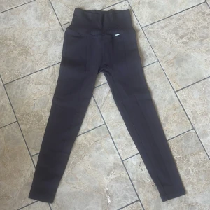 Bruna ribbade tights från Stronger - Säljer ett par bruna ribbade tights från Stronger med hög midja. Tightsen har en tight passform och är perfekta för träning. Materialet är stretchigt och bekvämt, med diskret logga framtill i midjan.