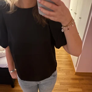 Svart satinblus med puffärm från Vila - Säljer en svart blus i satin från Vila med korta puffärmar. Blusen har en enkel, stilren design och rund halsringning. Perfekt att styla med jeans eller kjol för en trendig look.