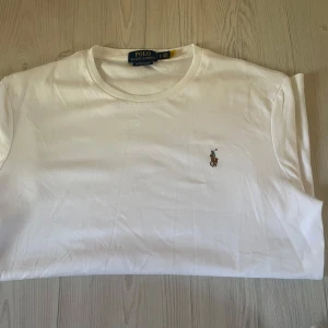 Polo Ralph Lauren || Custom Slim Fit  - Klassisk vit t-shirt från Polo Ralph Lauren med rund halsringning och broderad logga på bröstet. Tillverkad i mjuk bomull och har en normal passform. Perfekt basplagg med stilren design.
