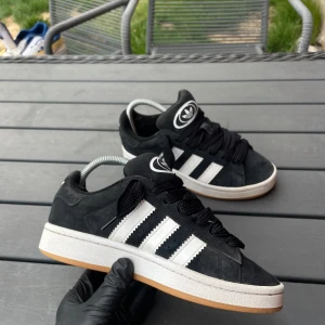 👟 ADIDAS Campus 00s – STRL 36 EU 👟 - 👟 ADIDAS Campus 00s – STRL 36 EU 👟 🖤 Snygga & Sköna – Grymt Pris! 🖤  ⚫️ Klassiska Adidas i svart mocka Tidlös design med vita ränder och brun yttersula. Sitter riktigt skönt på foten och passar till alla tillfällen.  ✅ Storlek: 36 EU / 22.5 CM Perfekta för dig med mindre fötter – snygga och bekväma!  🔍 Skick: Mycket bra – endast liten slitning vid hälen Enda lilla felet är en skavning vid hälen, men känns inte alls vid användning. I övrigt i mycket fint skick!  💵 Pris: 450 kr Prisvärda sneakers i