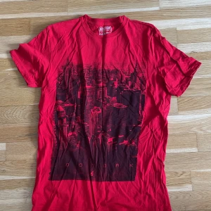 Röd t-shirt med stadsmotiv från Zoo York - Säljer en röd t-shirt från Zoo York med ett svart tryck av en stadssilhuett på framsidan. T-shirten har rund halsringning och är tillverkad i mjuk bomull.