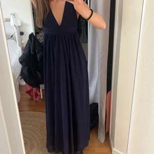 Mörkblå balklänning  med v-ringning - Storlek 32, supersnygg balklänning som aldrig blivit använd. Är 170 som referens !Säljer en elegant mörkblå långklänning med djup v-ringning och breda axelband. Klänningen har ett flytande fall och markerad midja, perfekt för festliga tillfällen. Materialet känns lätt och följsamt.