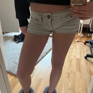 Beige jeansshorts med låg midja - Snygga beige jeansshorts med låg midja och klassiska fickor fram och bak. Shortsen har bälteshällor och stängs med knapp och dragkedja. Perfekta för varma dagar och en avslappnad stil.