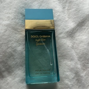 Dolce & Gabbana Light Blue Forever Pour Femme Eau de Parfum - En elegant parfym i en rektangulär glasflaska med turkosblå färg och gulddetaljer. Flaskan har ett stilrent utseende med blått lock och guldlist. Doften är en Eau de Parfum för kvinnor. Använd ca 1/5  eller mindre. 