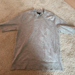 Grå kortärmad tröja från Lindex - Säljer en enkel och stilren grå tröja från Lindex i storlek XS. Tröjan har korta ärmar, rund halsringning och ribbade muddar vid ärmslut och nederkant. 