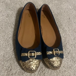 Blå ballerinaskor med glittrig tå och rosett - Mörkblå ballerinaskor med glittrig guld-tå, dekorerade med rosett och guldfärgat spänne framtill.💙