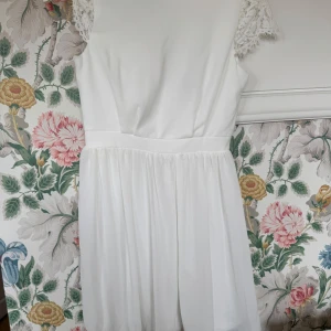 Vit klänning med spetsärmar - vit klänning med korta spetsärmar, rund halsringning, markerad midja och ett lätt, flödande kjolparti. Perfekt för somriga tillfällen eller studentfirande. Längd 90cm, midja 36. 