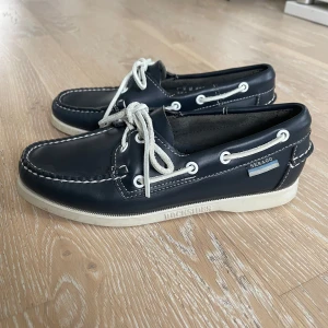 Stilrena Sebago Docksides – storlek 36 - Säljer ett par klassiska Sebago Docksides i storlek 36. Skorna är i mycket fint skick, knappt använda och väl omhändertagna. Perfekta till både vardag och sommarens lite finare tillfällen. Mörkblått skinn med vita detaljer och snören – en tidlös och snygg seglarsko som aldrig går ur tiden.  Nypris ligger runt 1200–1500 kr, mitt pris: 600 kr  Hör gärna av dig om du vill ha fler bilder eller har några frågor!