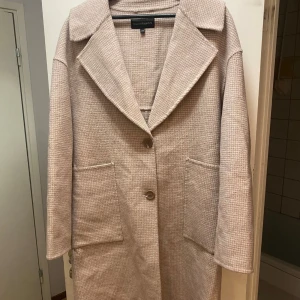 Beige lång kappa från KappAhl - Säljer en stilren beige kappa från KappAhl i storlek XS. Jackan har stora slag, två knappar framtill och rymliga fickor. Materialet är mjukt och har en diskret struktur. Perfekt för dig som vill ha en klassisk och tidlös look. Lite nopprig men går lätt att få bort med rakhyvel, därav priset 🌸