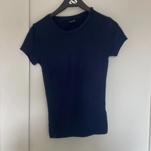 Mörkblå enkel t-shirt från gina - Säljer en mörkblå t-shirt med rund halsringning och korta ärmar. Modellen är figurnära och passar perfekt till jeans eller kjol. En klassisk baströja som funkar till det mesta.