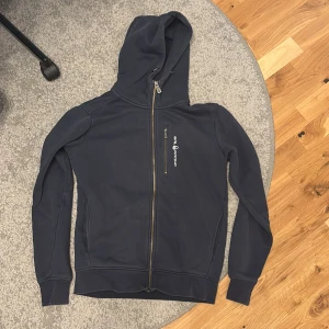 Mörkblå hoodie från Sail Racing - Säljer en mörkblå hoodie från Sail Racing med dragkedja och huva. Den är i princip oanvänd. Väldigt fint skick utan några täcken på användning. Vid snabb affär kan priset diskuteras. 