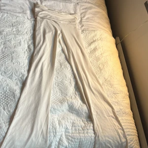 Vita utsvängda byxor från Gina Tricot - Säljer ett par vita utsvängda byxor från Gina Tricot i mjukt och stretchigt material. Byxorna har låga midja och sitter tight upptill med vidare ben nertill. Perfekta för en trendig och bekväm look.