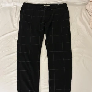 Svarta tygbyxor - Svarta, rutiga tygbyxor från DeFacto. Använda 2 gånger, i felfritt skick. Storlek 34/32 men har ett snöre i midjan för att kunna anpassa dom