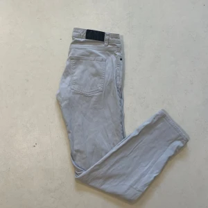  Dressmann jeans  - Säljer ett par ljusgrå chinos från Dressmann i regular fit. Byxorna har klassiska fickor och en enkel design som passar till många olika stilar. Perfekta för dig som gillar en stilren look.