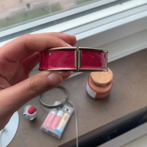 Rött armband med guldfärgade kanter - Säljer ett snyggt armband i röd färg med guldfärgade kanter. Armbandet har en stilren och modern design som passar perfekt för att lyfta din outfit.