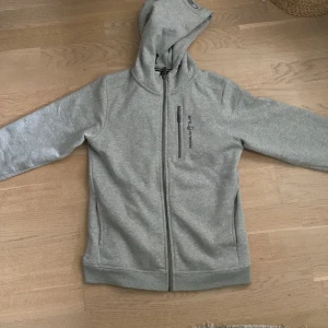 Grå hoodie från Sail Racing - Säljer en grå hoodie från Sail Racing med dragkedja skick 10/10 inga defekter alls. Strl 170. Köparen står för frakten själv.
