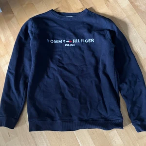 Mörkblå sweatshirt från Tommy Hilfiger - Säljer en mörkblå sweatshirt från Tommy Hilfiger med broderad logga och texten 'EST. 1985' på bröstet. Perfekt för en stilren och avslappnad look.