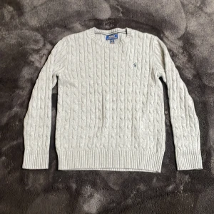 Ljusgrå kabelstickad tröja från Polo Ralph Lauren - Säljer en ljusgrå kabelstickad tröja från Polo Ralph Lauren. Tröjan har rund halsringning, långa ärmar och klassisk kabelstickad struktur. Liten broderad logga på bröstet. Perfekt för lager-på-lager och stilren look. Barnstorlek,passar dig som har storlek 158/164