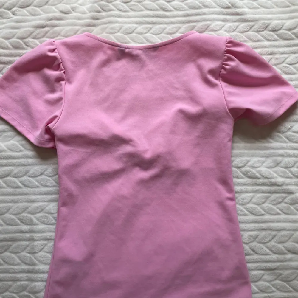 Säljer en söt rosa topp från Vero Moda med korta puffärmar och snygg knutdetalj framtill. Toppen har en djupare urringning och är tillverkad i mjuk bomull. Perfekt för dig som vill ha en feminin och trendig look!💞💞liten i storleken 💞. Yläosat.