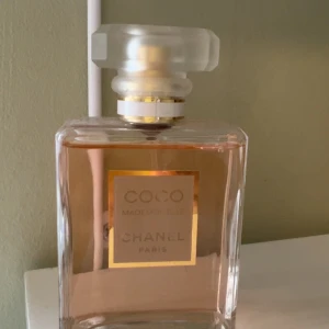 Coco Mademoiselle Eau de Parfum från Chanel - Elegant parfymflaska med ljusrosa vätska från Chanel. Coco Mademoiselle Eau de Parfum har en klassisk, fyrkantig glasflaska med frostad, geometrisk kork och gulddetaljer. Doften är känd för sin fräscha och sofistikerade karaktär. Pris är diskuterat bart