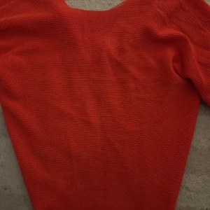 Röd stickad tröja med twist från Mango - Säljer en röd stickad tröja från Mango med snygg twist-detalj i ryggen. Tröjan har lång ärm och är i ett mjukt, ribbat material. Perfekt för dig som vill ha något färgstarkt och trendigt i garderoben!