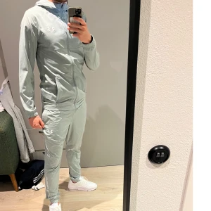 Grå träningsbyxor från Under Armour - Snygga mint gröna tracksuit från Under Armour med logga på låret och text längs benet, och på ryggen på jackan. Byxorna har normal passform och tröjan har normal passform. Tillverkade i syntetmaterial som andas och ger bra rörelsefrihet. Byxorna är storlek S och jackan M, personen på bilden är 180cm! Setet Köpt för 1850kr!