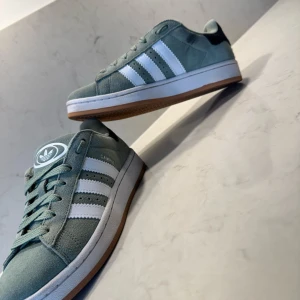 Adidas Campus  - Snygga Adidas Campus sneakers i ljusgrön mocka med klassiska vita ränder och vit sula. Perfekta för dig som gillar en stilren och sportig look. I princip helt nya använts 2-3 gånger skicket är där med 9/10